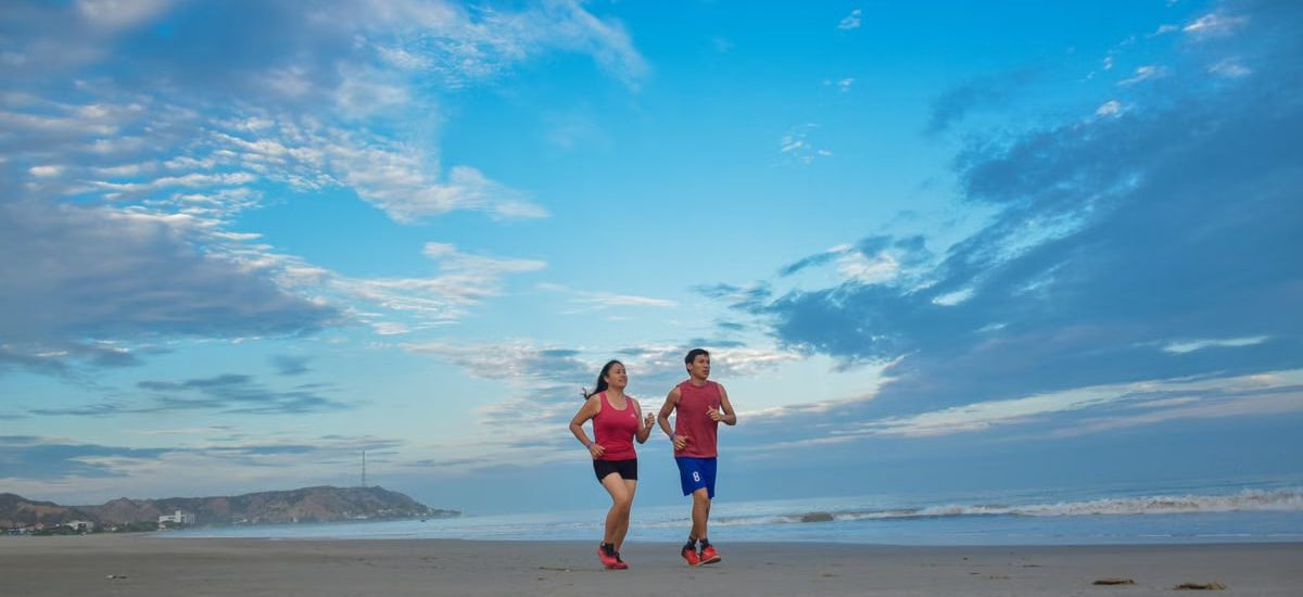A couple enjoys jogging together along a scenic beach under a bright blue sky.